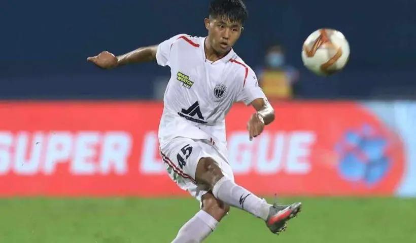 Photograph of Apuia, a person with long hair, wearing a traditional attire and standing against a backdrop of foliage.