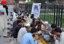 A group of people, including men, women, and children, are sitting together on the ground and having food in an open field.