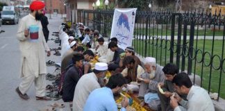 A group of people, including men, women, and children, are sitting together on the ground and having food in an open field.