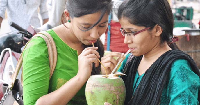 Indian girl drinking coconut water as a solution to contaminated road water