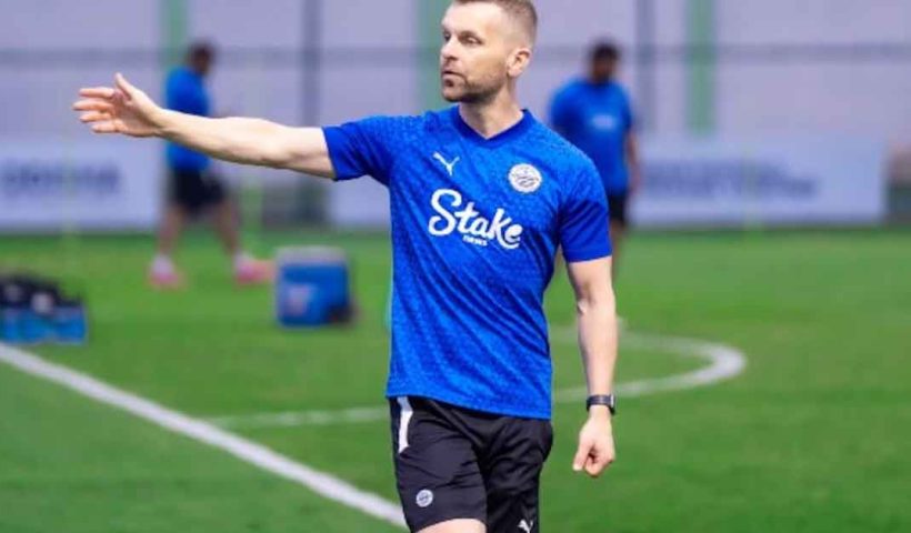 Image of Mumbai City FC Coach Petr Kratky, a man wearing a team tracksuit and cap, standing on a football field with a determined expression
