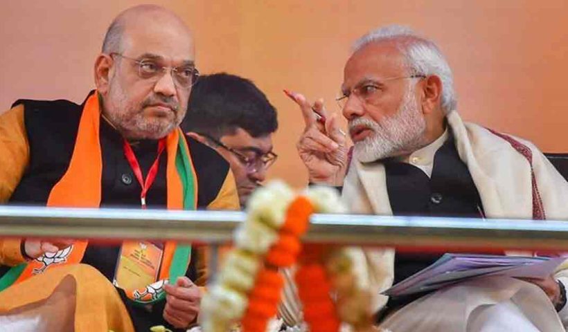 Two BJP Leader, Narendra Modi and Amit Shah, standing together in a political setting, discussing or addressing a crowd