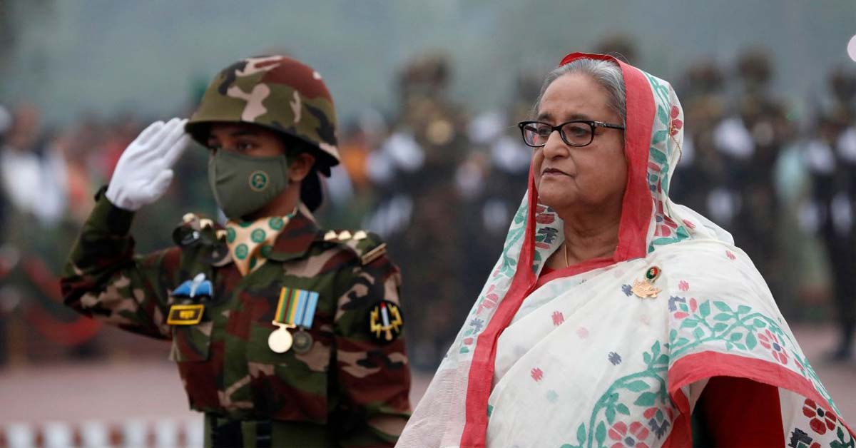 Bangladesh Prime Minister Sheikh Hasina giving a serious address or warning. She is dressed in traditional attire, and the image captures her with a focused expression, likely speaking at an official event or press conference.